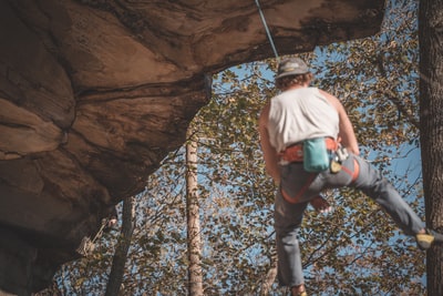 A man wearing a white vest and blue denim jeans climbed a brown rock strata in the daytime
